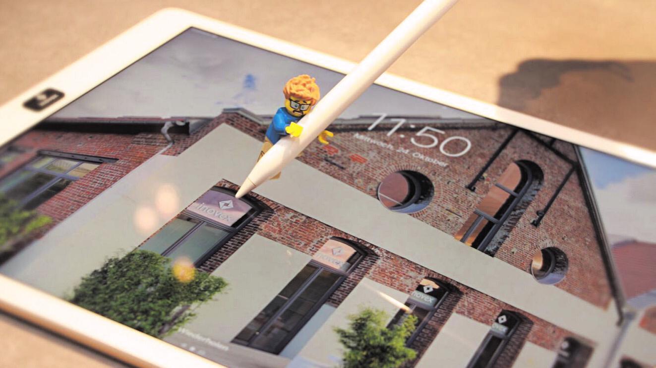 A Lego figure holding an Apple Pencil on top of an iPad showing an office.