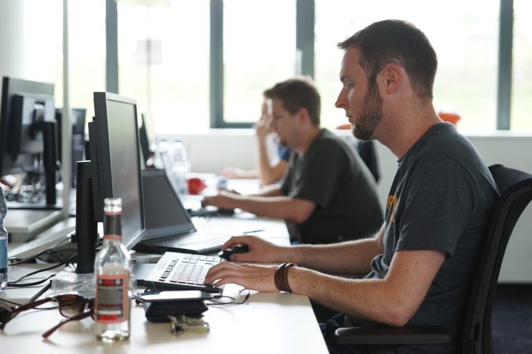 Drei Männer sitzen am Schreibtisch und arbeiten vor Ihren Bildschirmen.
