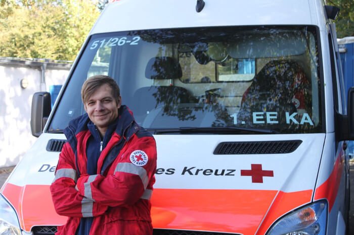 Ein Mann in DRK-Uniform steht vor einem DRK-Fahrzeug