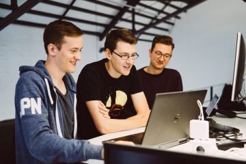 Drei Männer gucken gemeinsam auf Laptop
