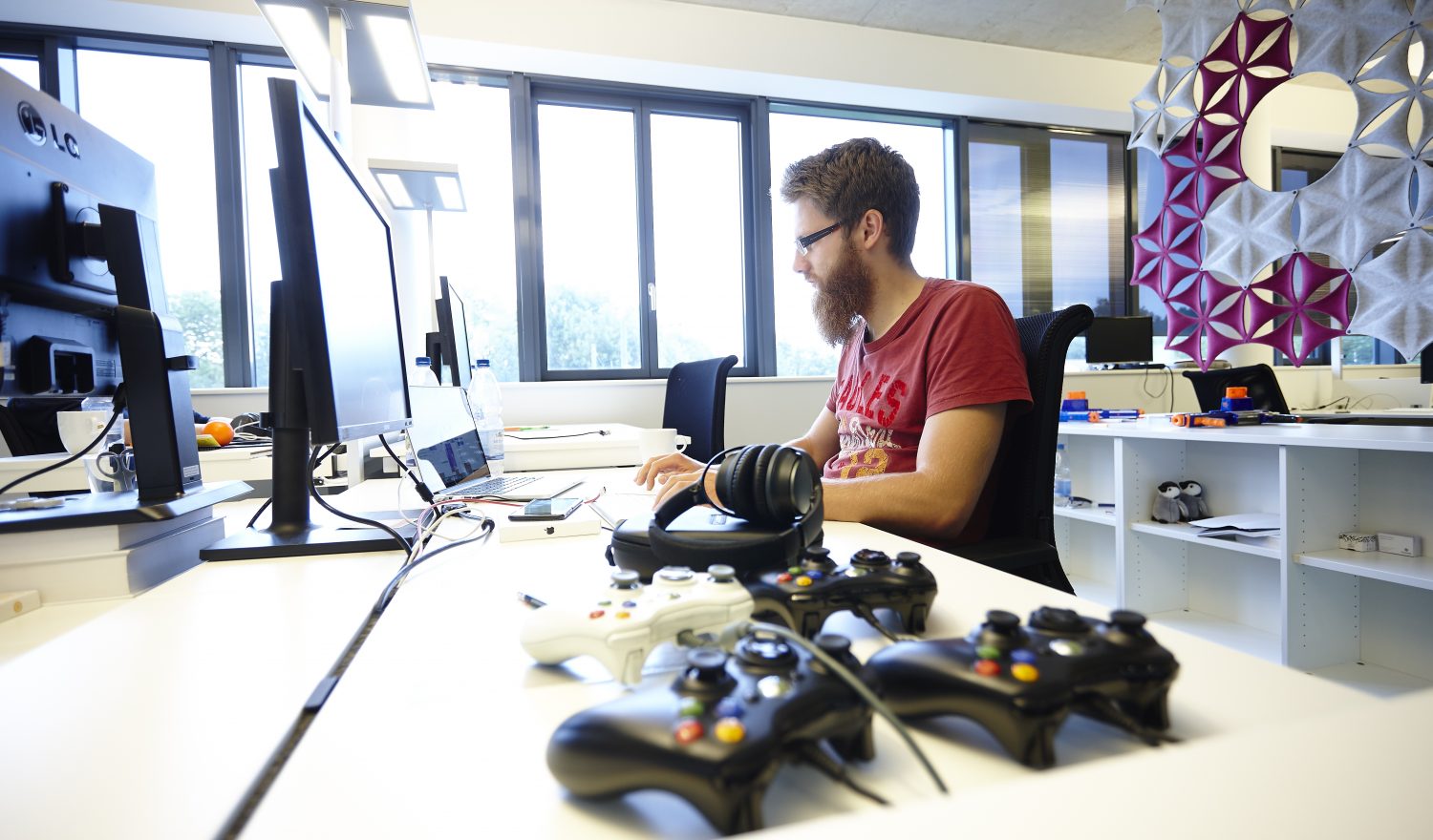 Ein Kollege arbeitet im Großraumbüro. Auf seinem Paltz liegen Controller.