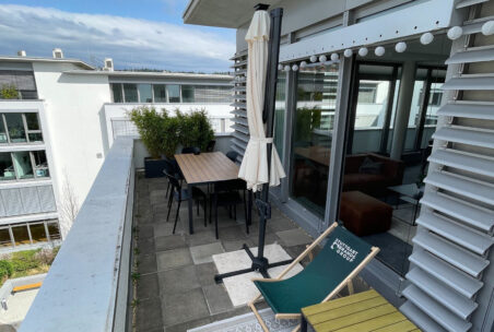 Terrasse mit Sonnenstuhl und eingeklapptem Sonnenschirm.