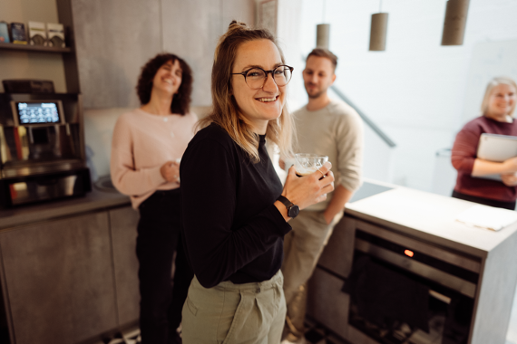 4 Menschen stehen lächelnd in einer Küche, zwei Personen halten eine Kaffeetasse