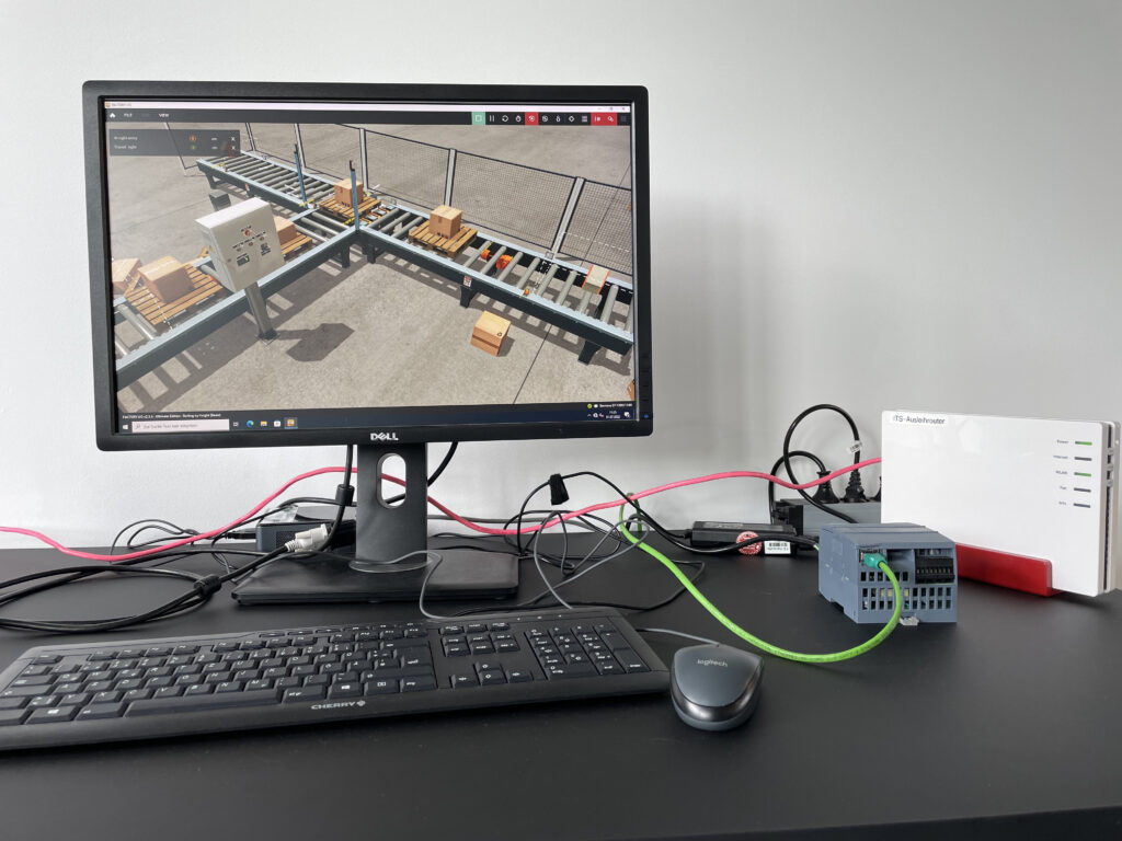 Ein Computerbildschirm zeigt die Simulation einer Paketförderanlage. Daneben steht eine kleine SPS, die mit einem LAN-Kabel mit dem Computer verbunden ist.