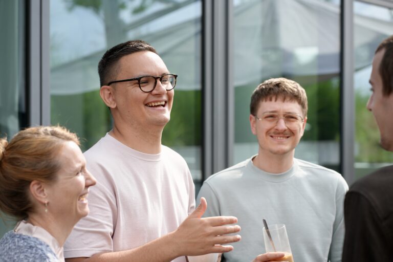 Mehrere Menschen mit Getränken in den Händen stehen in einer Gruppe zusammen, lachen und unterhalten sich.