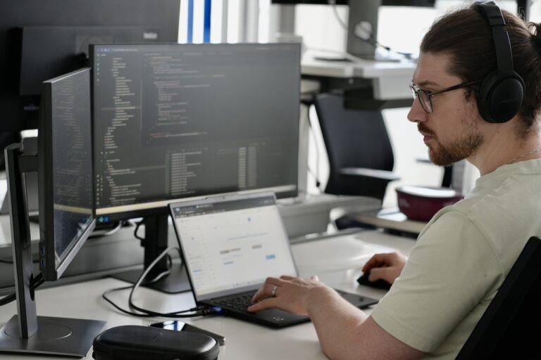 Eine Person arbeitet konzentriert mit Kopfhörern auf vor mehreren Bildschirmen.