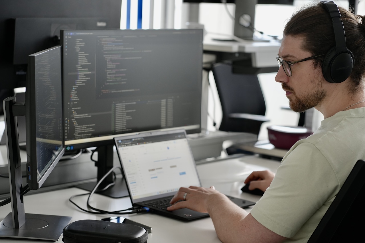 Eine Person arbeitet konzentriert mit Kopfhörern auf vor mehreren Bildschirmen.