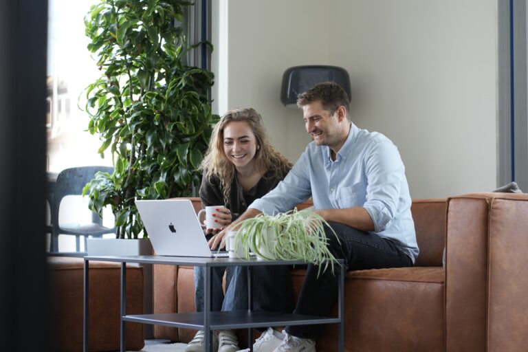 Zwei Personen sitzen auf einem Sofa und schauen auf einen Laptop.