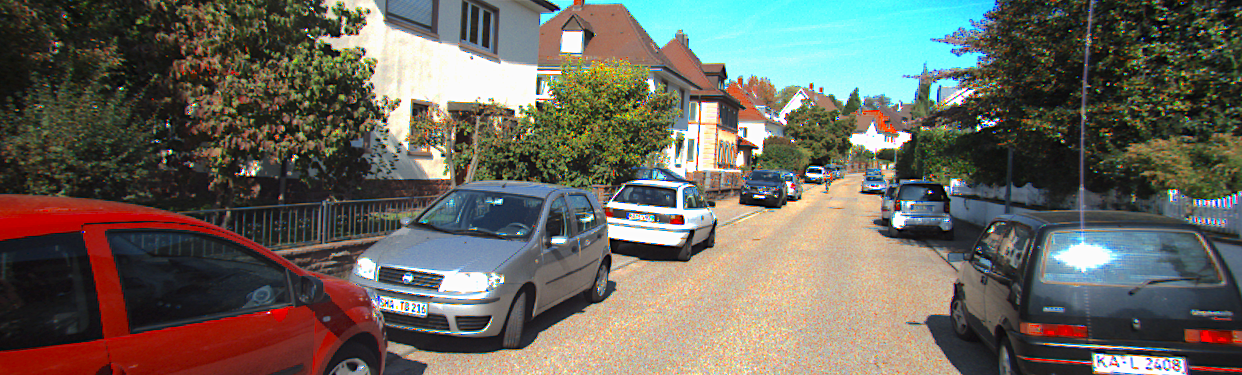 An image from the KITTI dataset that shows a street in a residential area where cars park on the side.