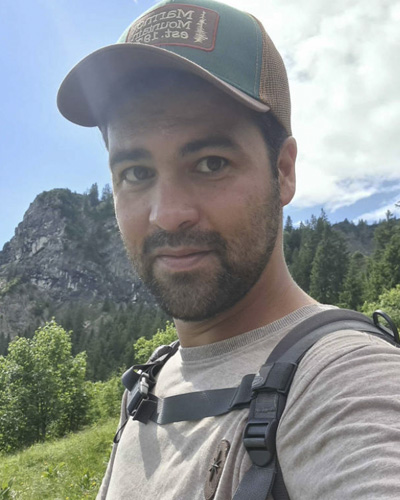 Marcello Pauli mit Cap vor Berggipfel mit Bäumen und Wiese