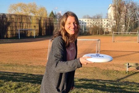 Frau mit Frisbee vor Fußballfeld