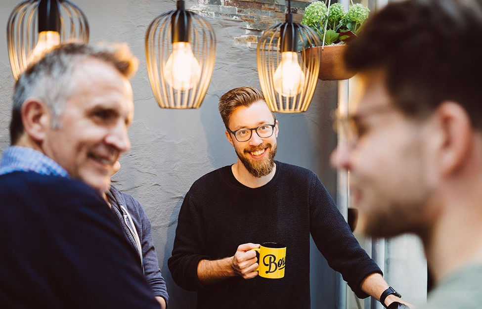 Drei positive Männer, ein Mann hält einen Kaffebecher in der Hand
