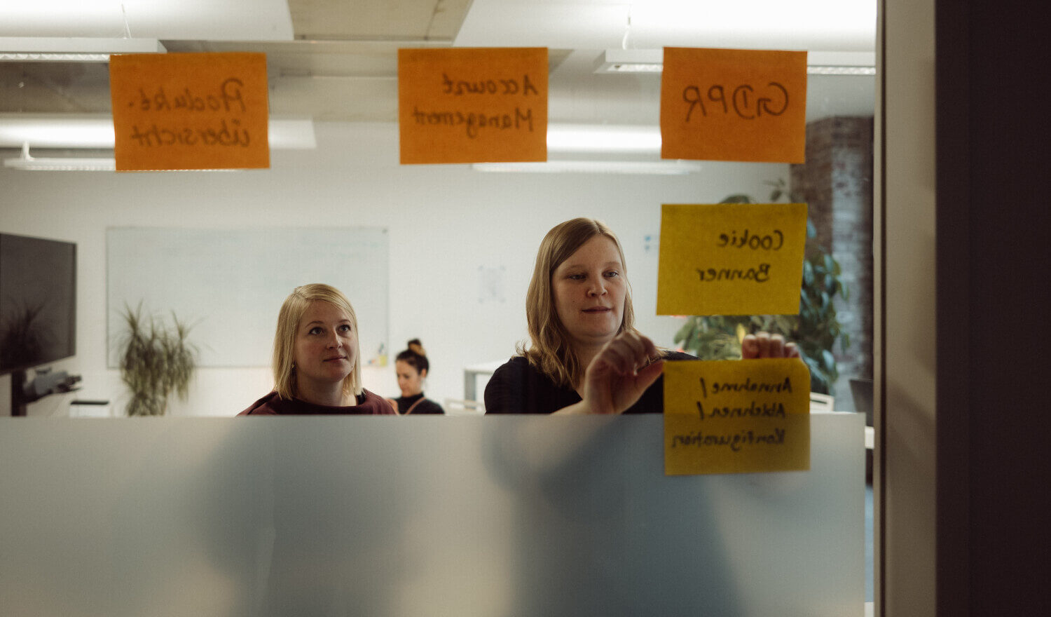 Zwei Frauen kleben Post-Its an ein Glasfenster
