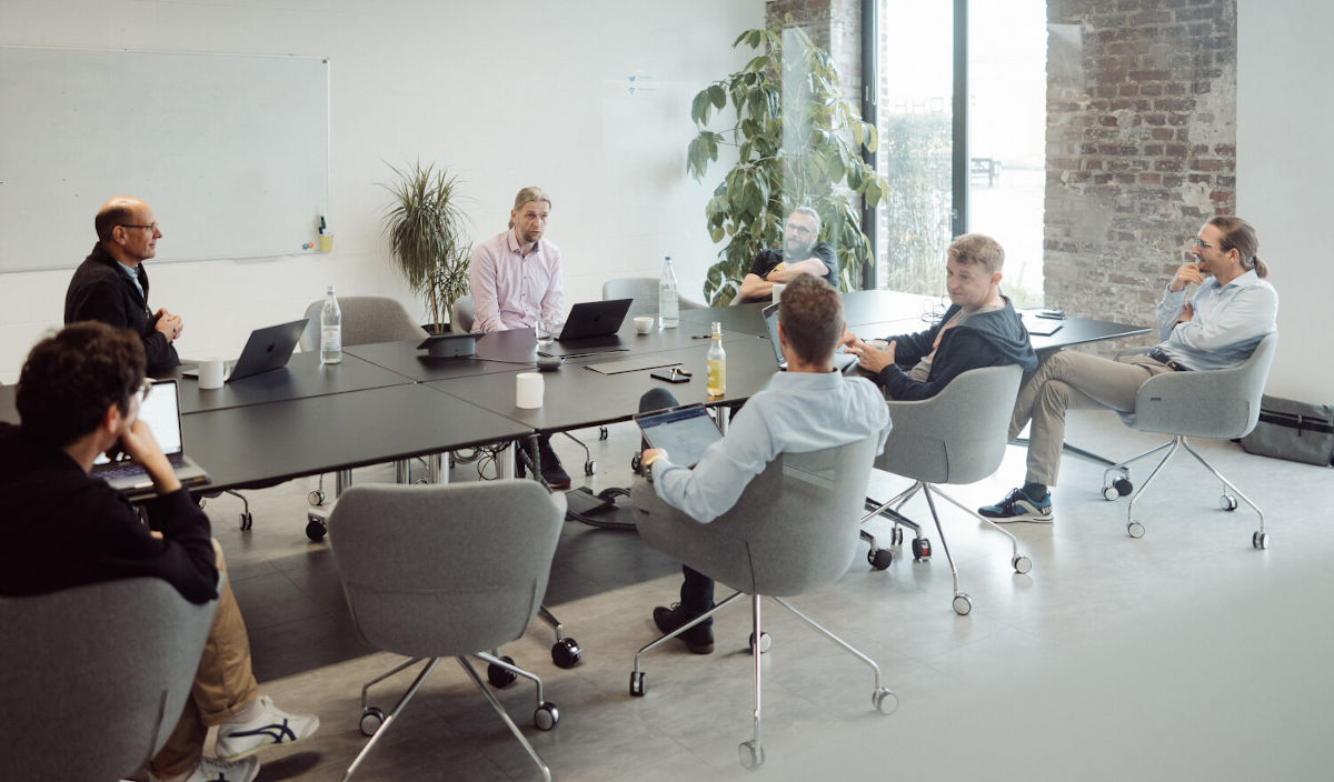 Sieben Menschen sitzen an einem Konferenztisch und diskutieren