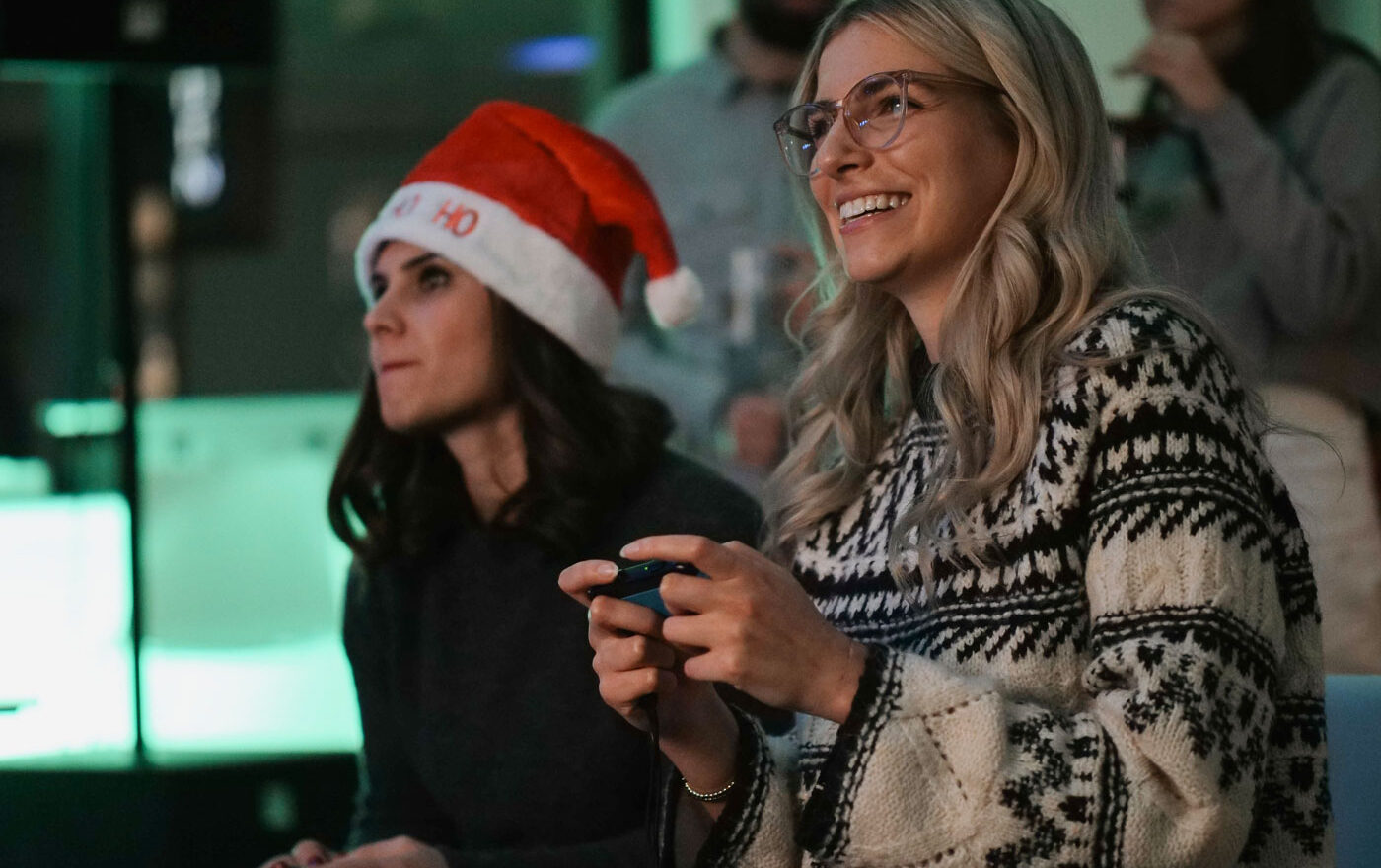 Zwei Menschen stehen nebeneinander und spielen mit einer Console. Eine der beiden Personen trägt eine Weihnachtsmütze.