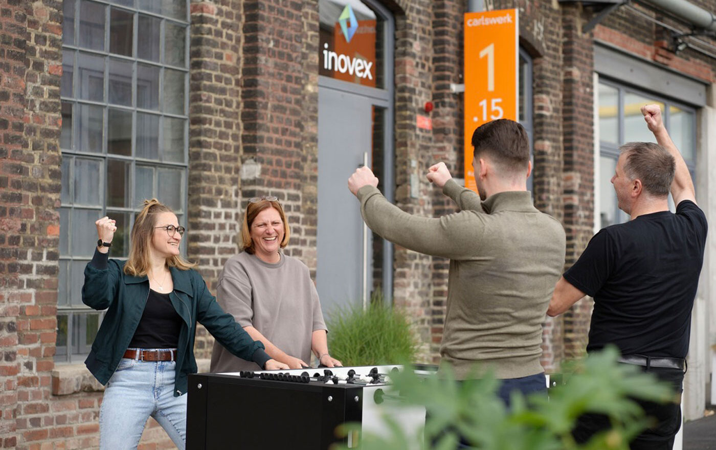 Vier Menschen spielen Tischkicker und lachen.